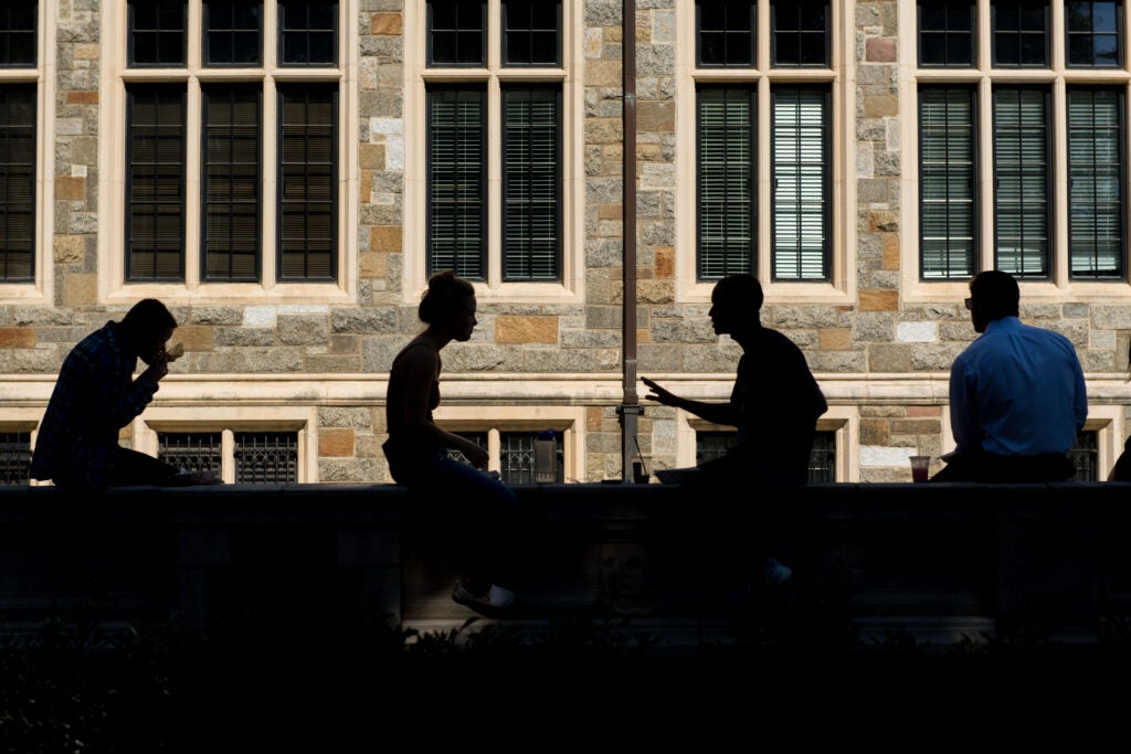 Silhouetted students sitting on ledge outside of campus building