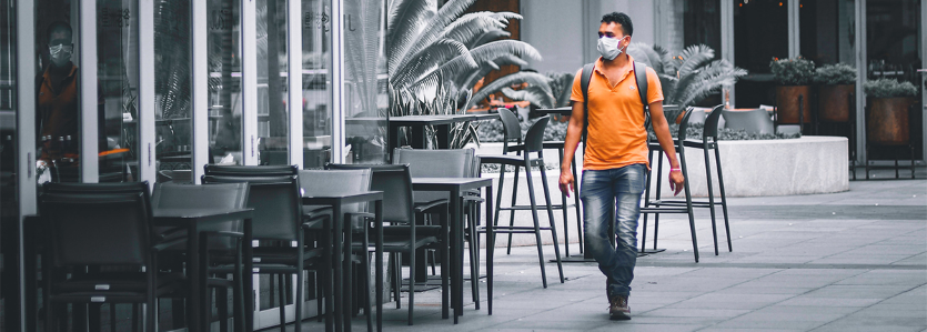 man in orange shirt wearing mask walking past empty tables