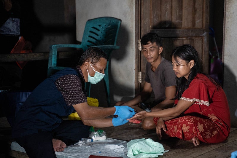 Healthcare worker draws a blood sample from a girl's finger to test for lymphatic filariasis